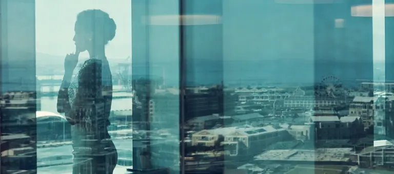 A thoughtful woman looking out of an office window over the city skyline
