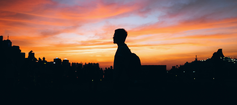 Silhouette of man in front of cityscape against sky during sunset