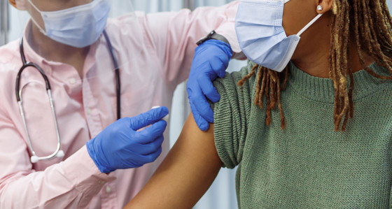 A woman with facemask is getting vaccinated by a person wearing PPE