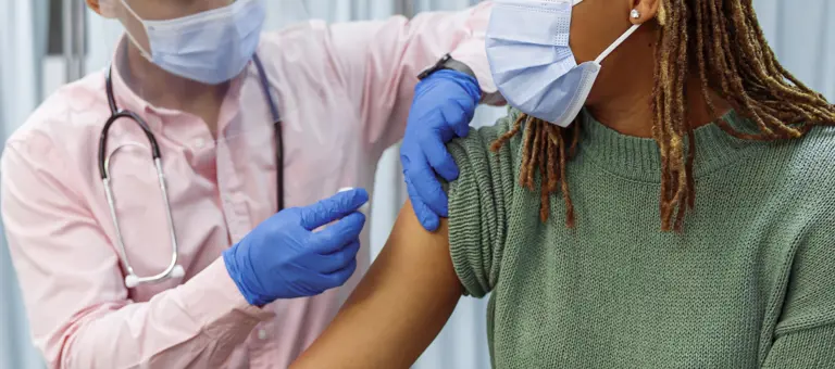 A woman with facemask is getting vaccinated by a person wearing PPE