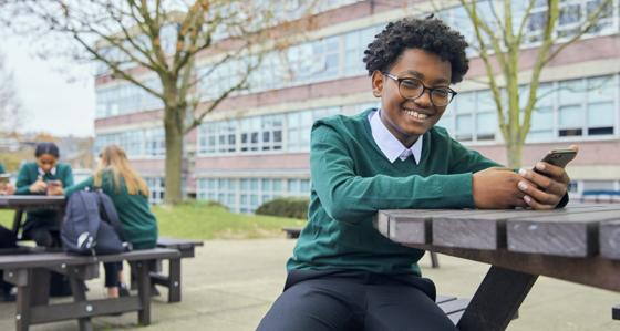 Child at school smiling while holding a smartphone