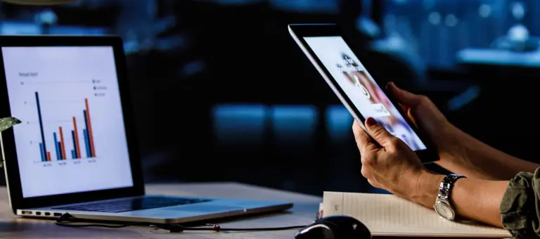 Woman in an office looking at reports on her laptop and tablet