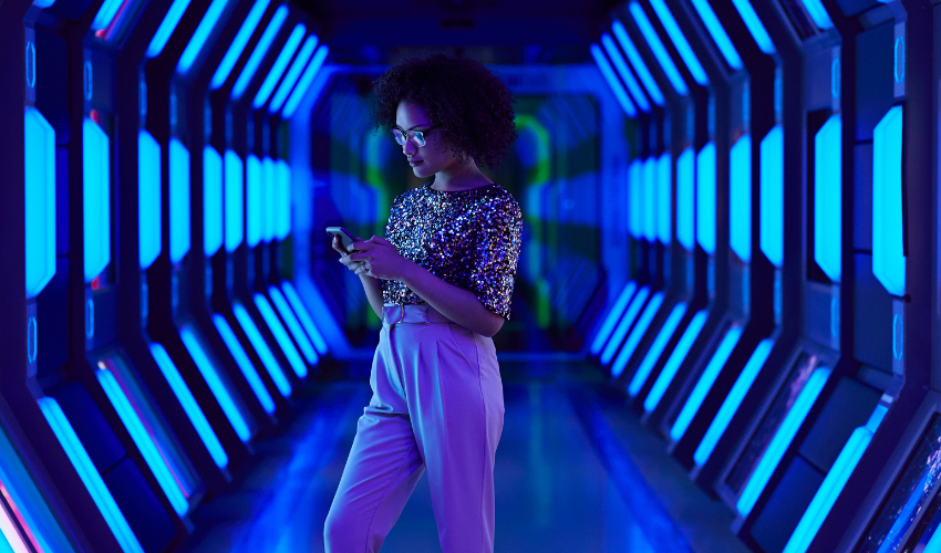 A person in a sequined top uses a phone in a futuristic, neon-lit blue hallway