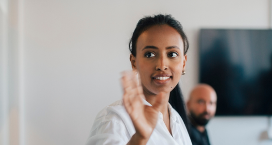 A woman waving while colleagues look on in the background of an office setting