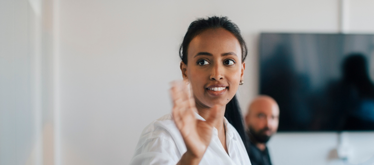 A woman waving while colleagues look on in the background of an office setting