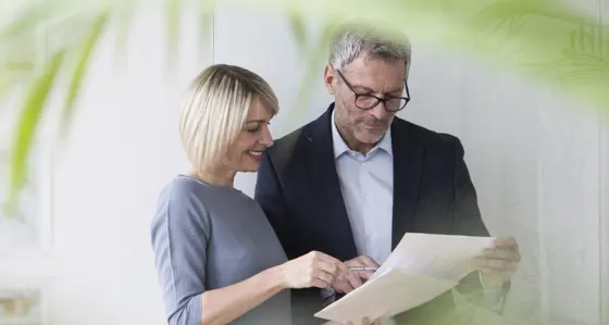 Two people looking at a piece of paper with a palm frond in the foreground