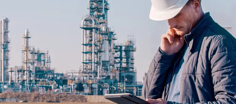 A man wearing a hard hat standing in front of an industrial landscape