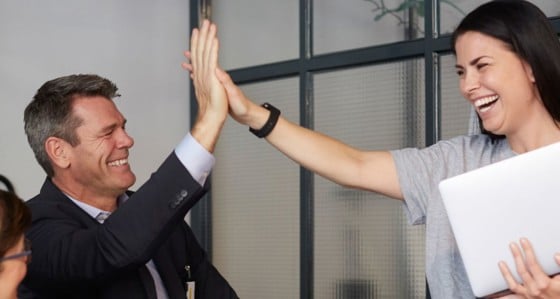Cheerful creative businesswoman high-fiving with male bank manager during meeting in office