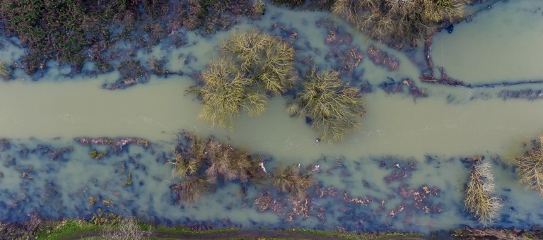 An aerial view of a muddy flooded river that has burst its banks