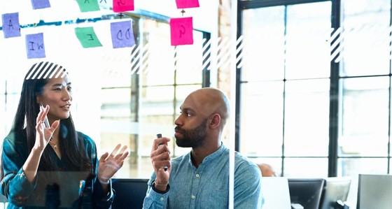 A man and woman discussing post-its on a transparent office wall