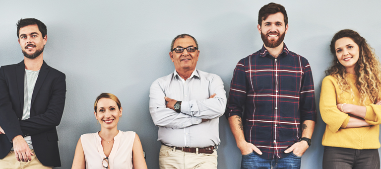 Seven smiling people in front of a grey wall