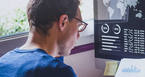 A man reading paper data reports and stocks graphs on his computer