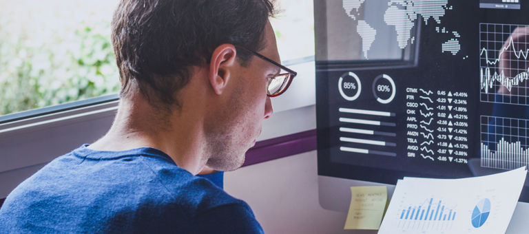 A man reading paper data reports and stocks graphs on his computer