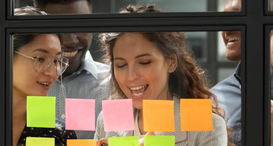 Four people looking at post its on a glass interior window