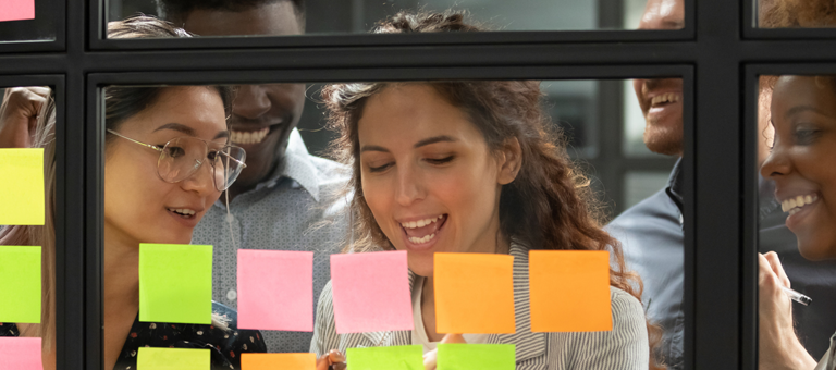 Four people looking at post its on a glass interior window