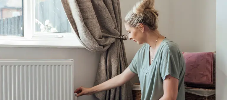 A woman adjusting a radiator in her home
