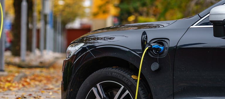 A black electric car charging in a leafy street