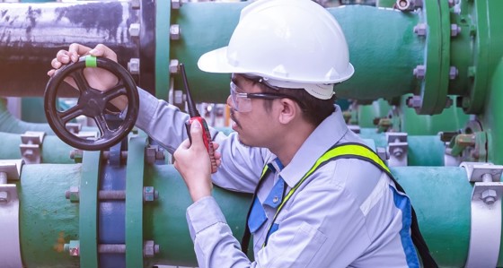 An engineer on a walkie talkie inspecting the valve of a pipe