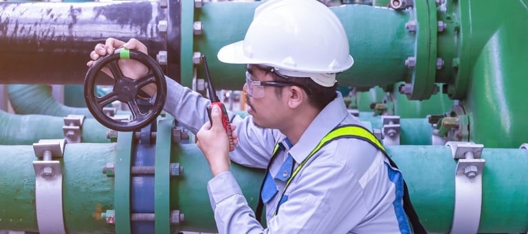 An engineer on a walkie talkie inspecting the valve of a pipe