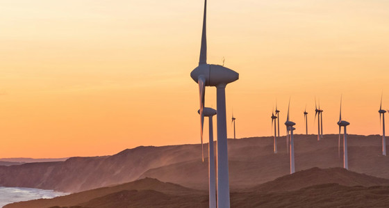 A windfarm in hills front of orange skies