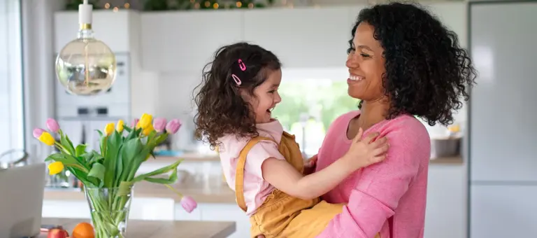 A woman holding a child in her arms inside her home
