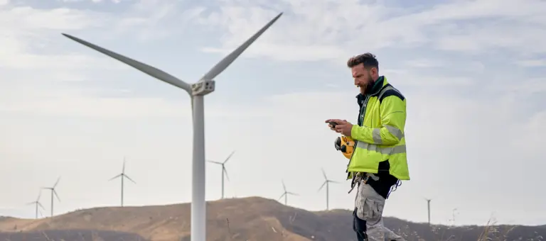 A man looking at his phone at a windfarm