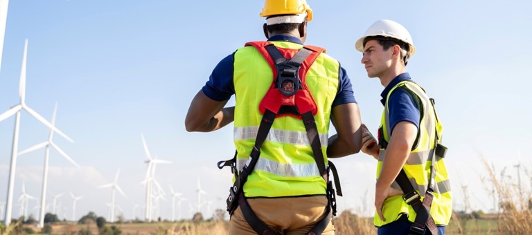 Two maintenance men wearing harnesses at a windfarm
