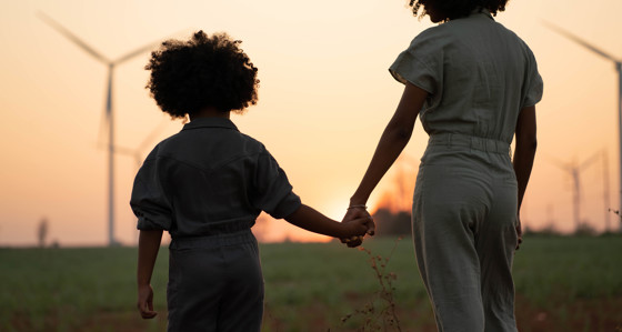 Two people holding hands in front of wind turbines at sunset