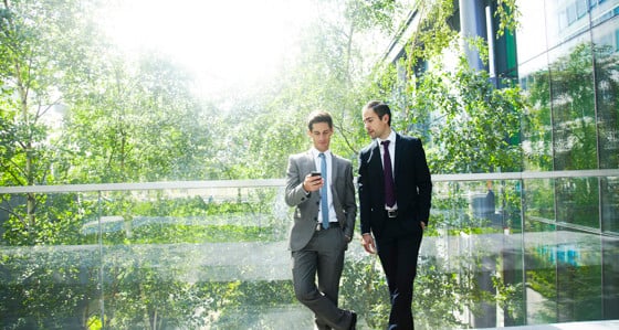 Two men looking at a phone while standing on a balcony in front of trees