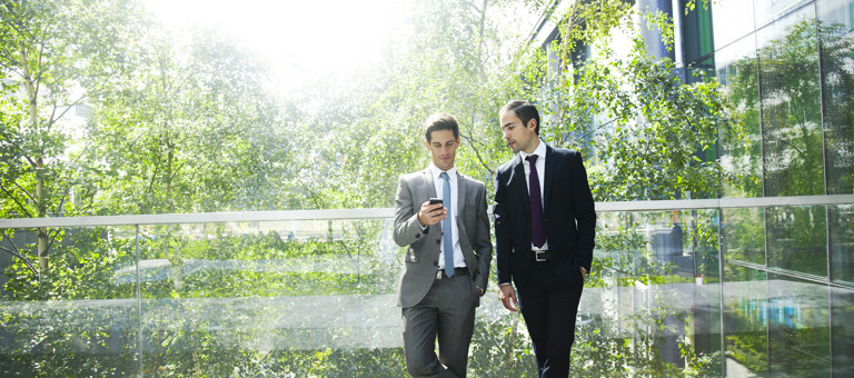 Two men looking at a phone while standing on a balcony in front of trees