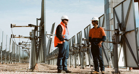 Two men in hard hats chatting in a solar panel farm