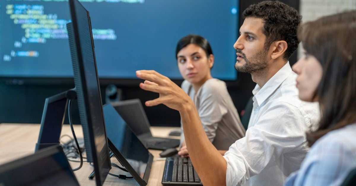 Group of people in a meeting with a screen showing coding in the background