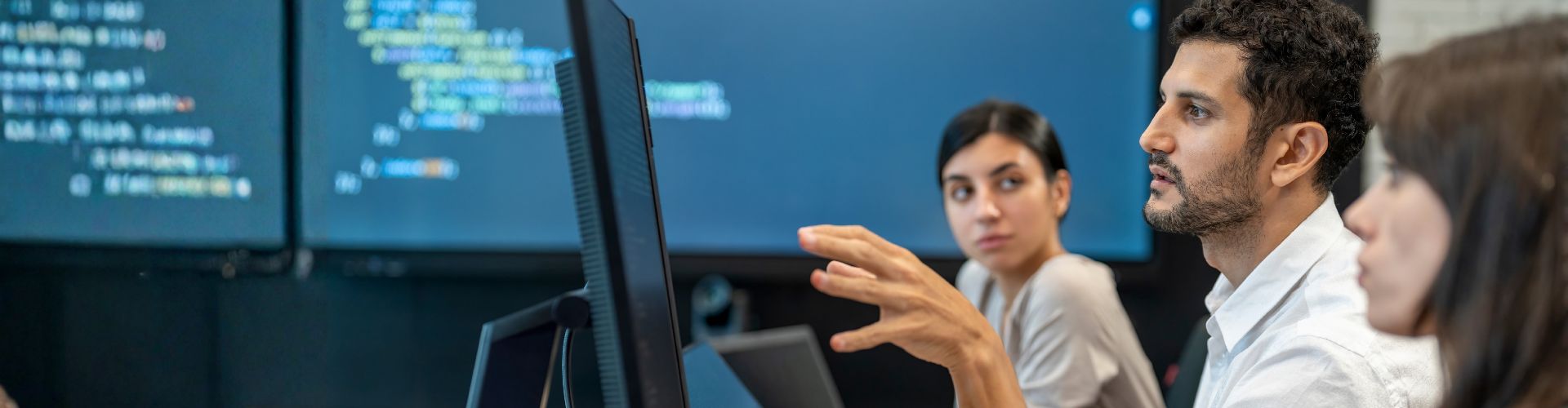 Group of people in a meeting with a screen showing coding in the background
