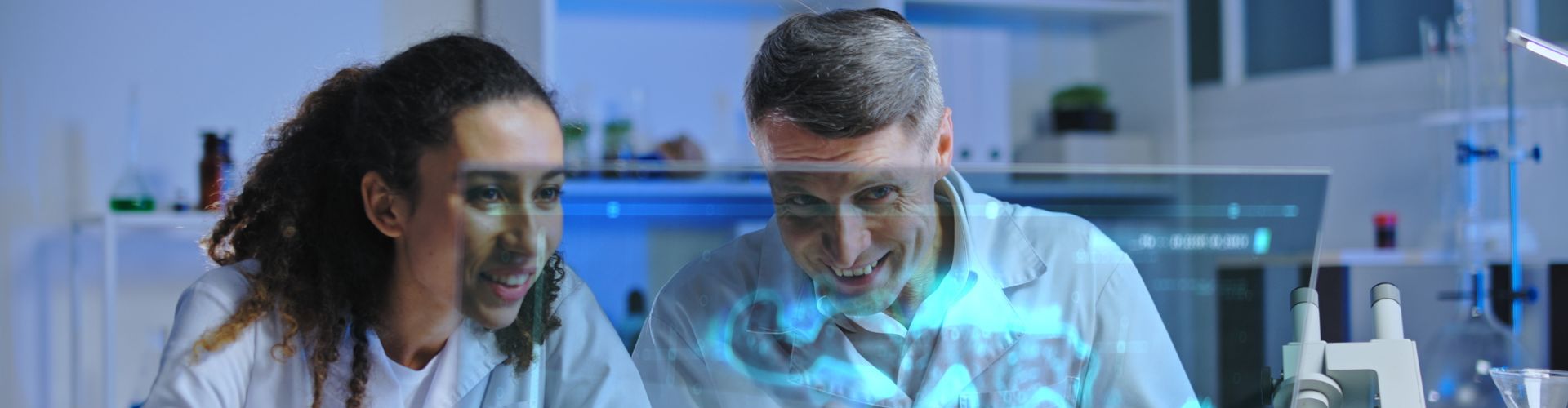 Two people in lab coats looking at a monitor