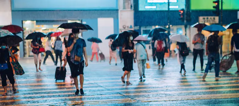 Crowd of people carrying umbrellas crossing the street in heavy rain at night