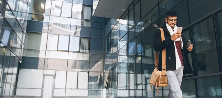 Man walking outside glass building using his mobile phone