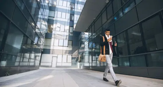 Man walking outside glass building using his mobile phone