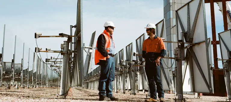 Two men in hard hats chatting in a solar panel farm