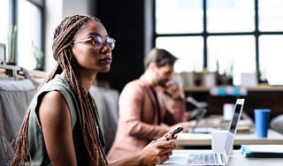 A black woman in glasses with braided hair sitting in front of a laptop