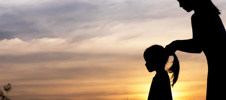 A mum putting her daughter's hair in a pony-tail silhouetted by the setting sun
