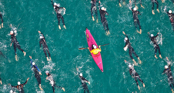 A pink kayak paddling among wet-suited sea swimmers