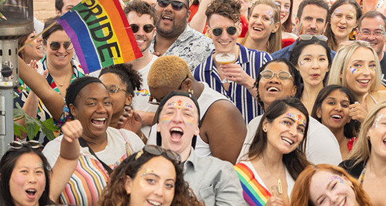 A group of smiling people with Pride rainbow flags