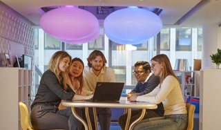 Five colleagues sitting around a laptop in a relaxed office environment