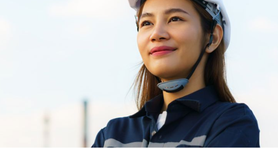A woman in a hard hat with an industrial landscape in the background