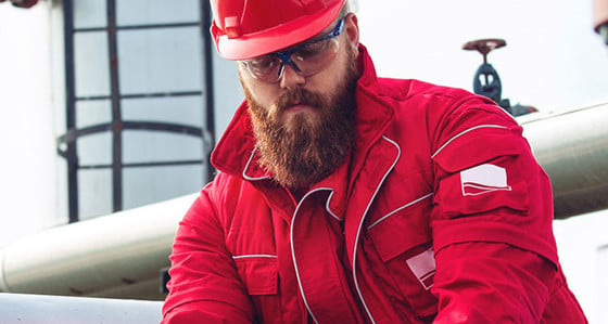 A bearded man in a hard hat working on some large pipes