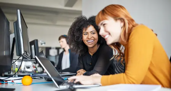 Two interns laughing together while working at their laptops