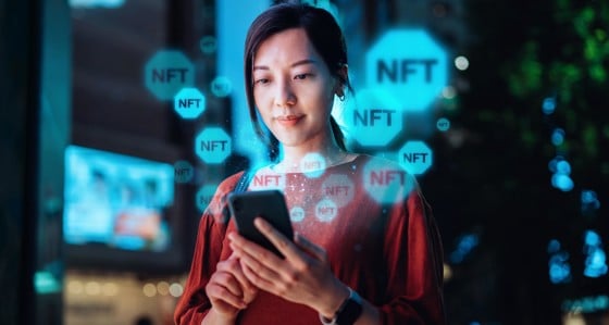 A woman looking at smart phone with an overlay of NFT logos