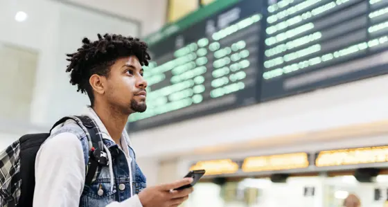 Young man at the airport looking at the list of destinations holding a cell phone