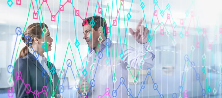 Two colleagues discussing data on a transparent wall in front of them
