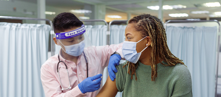 A woman wearing a facemask receiving a vaccine from someone in PPE